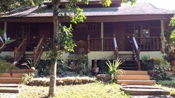 A traditional wooden house with a tiled roof, a wooden staircase, and a well-maintained garden with various plants and a stone pathway.