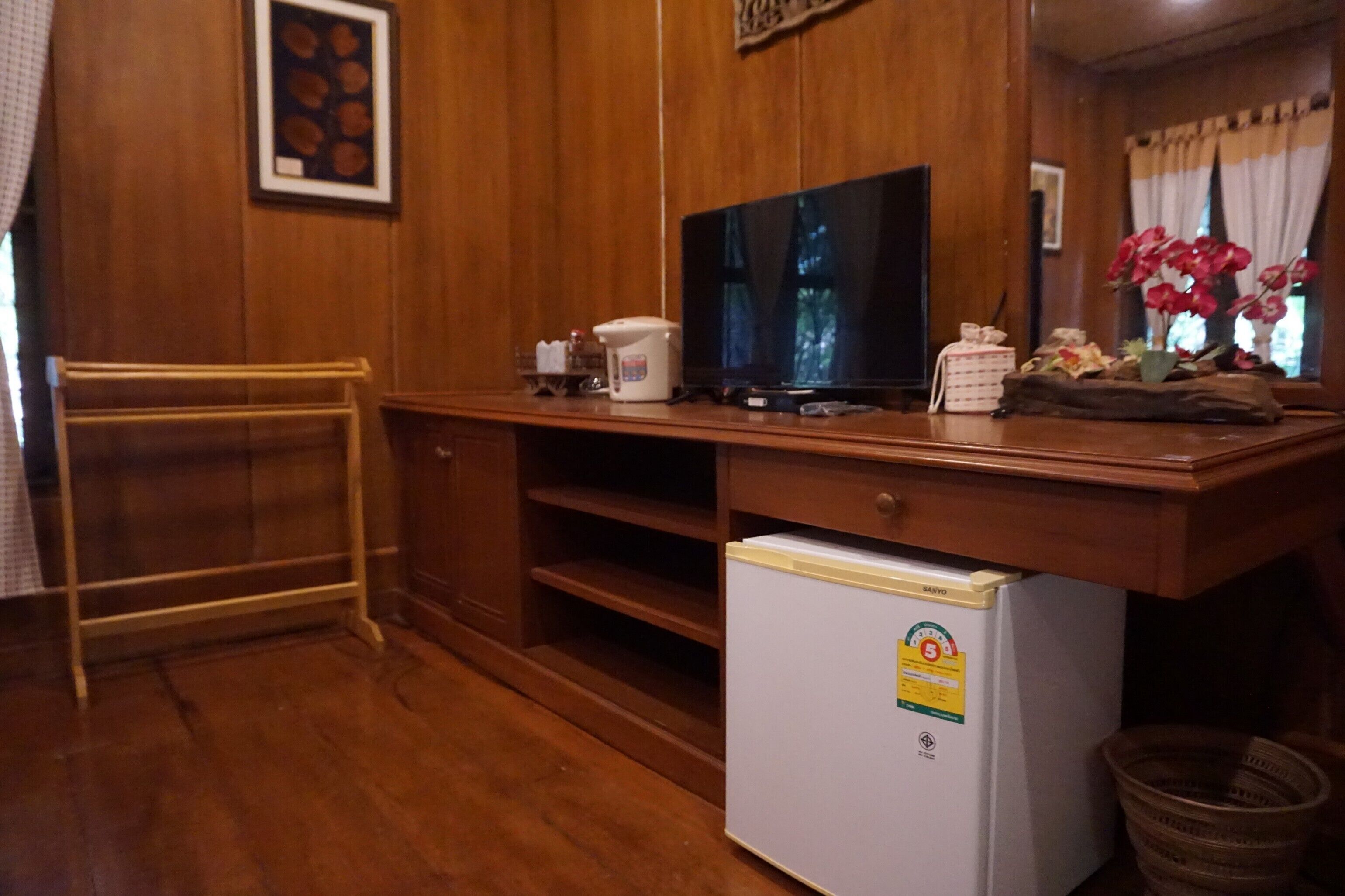 A compact room with wooden walls, a television on a wooden stand, a small refrigerator, and a window with curtains.