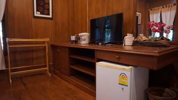 A compact room with wooden walls, a television on a wooden stand, a small refrigerator, and a window with curtains.