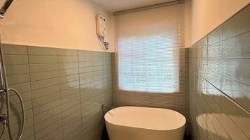 A bathroom with a freestanding bathtub, a handheld showerhead, and a wall-mounted control panel.
