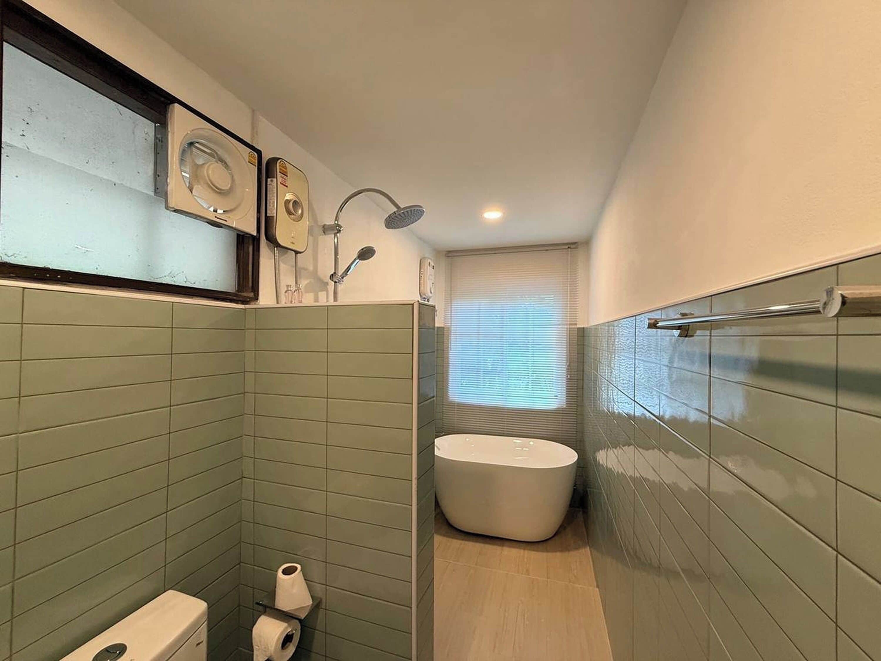 A compact bathroom with green tiles, a toilet, a bidet, a shower, and a bathtub.