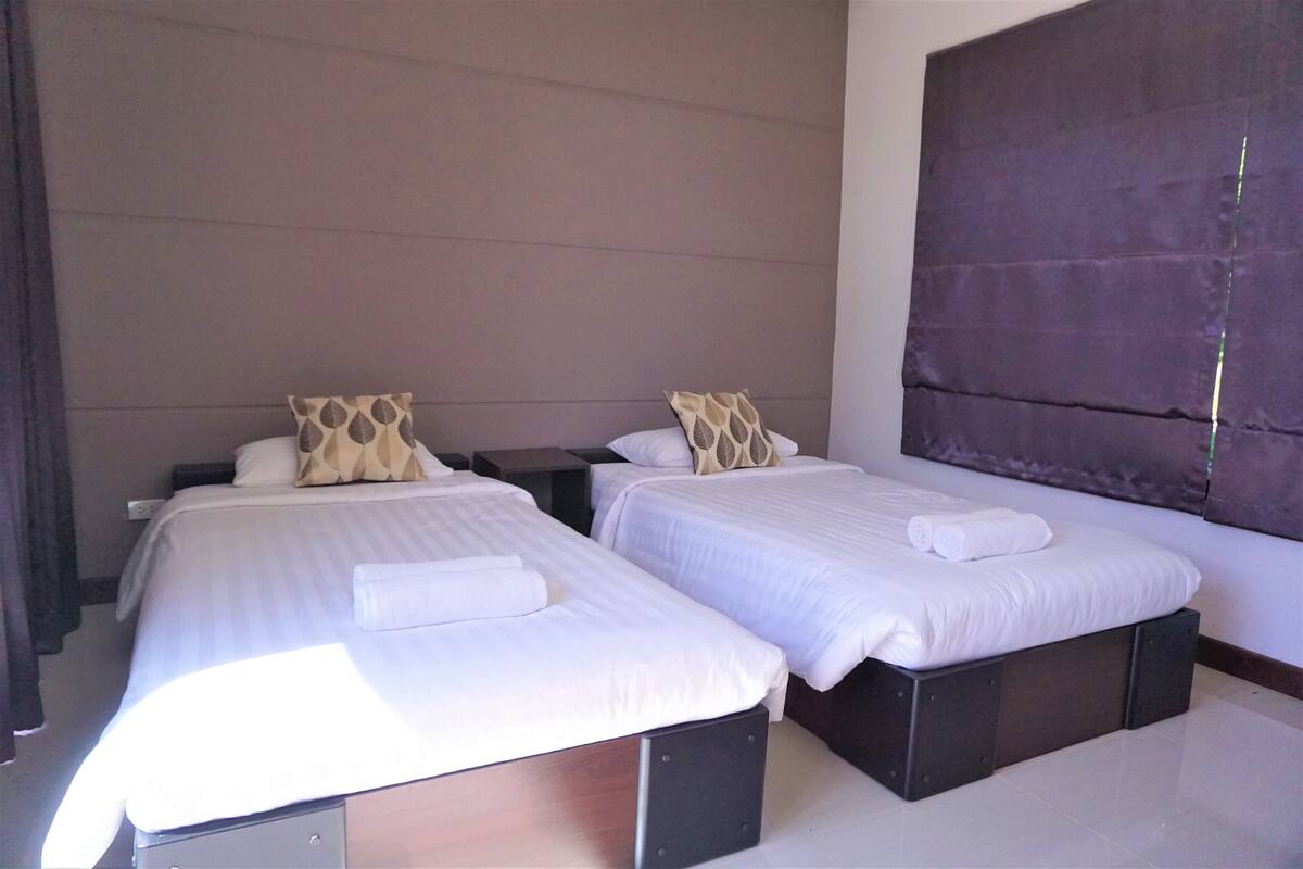 A hotel room with two single beds, each with a pillow and a rolled towel.