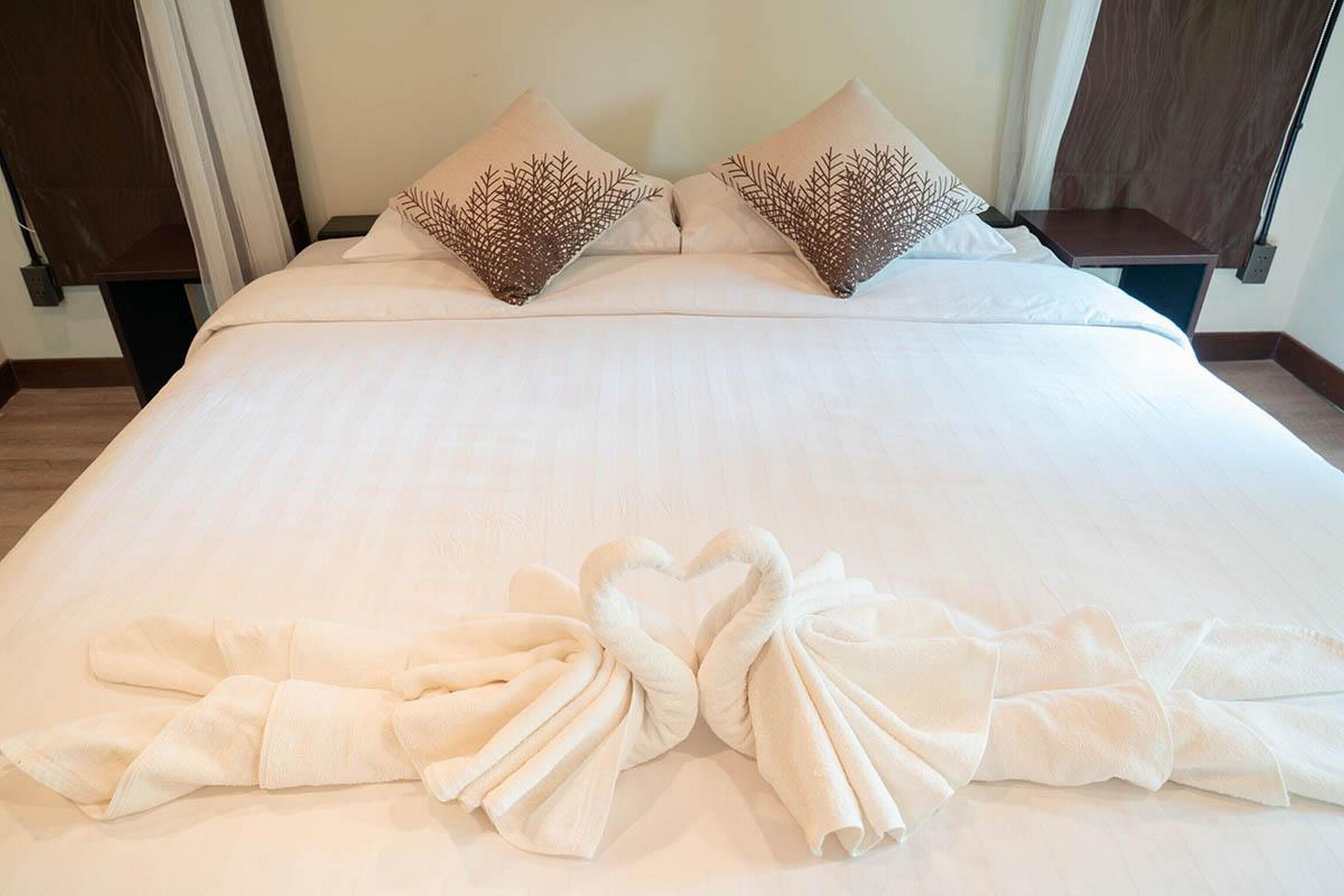 A neatly made bed with white linens and decorative pillows, a wooden headboard, and a pair of towels arranged on the bed.