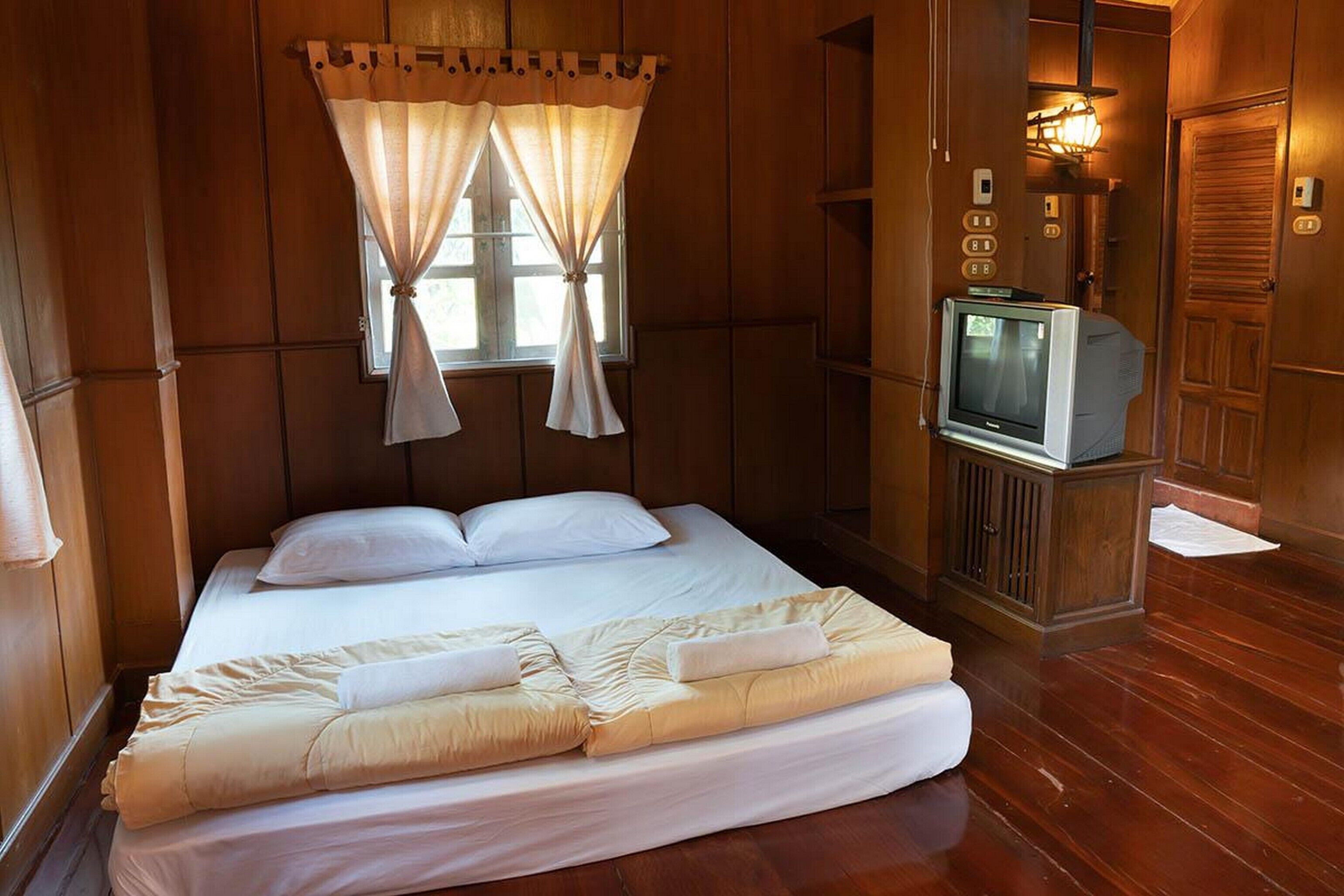 Habitación con paneles de madera, una cama, televisor y ventana con cortinas.
