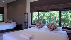 Habitación de hotel con dos camas, un ventanal con vistas a árboles y un cabecero oscuro.