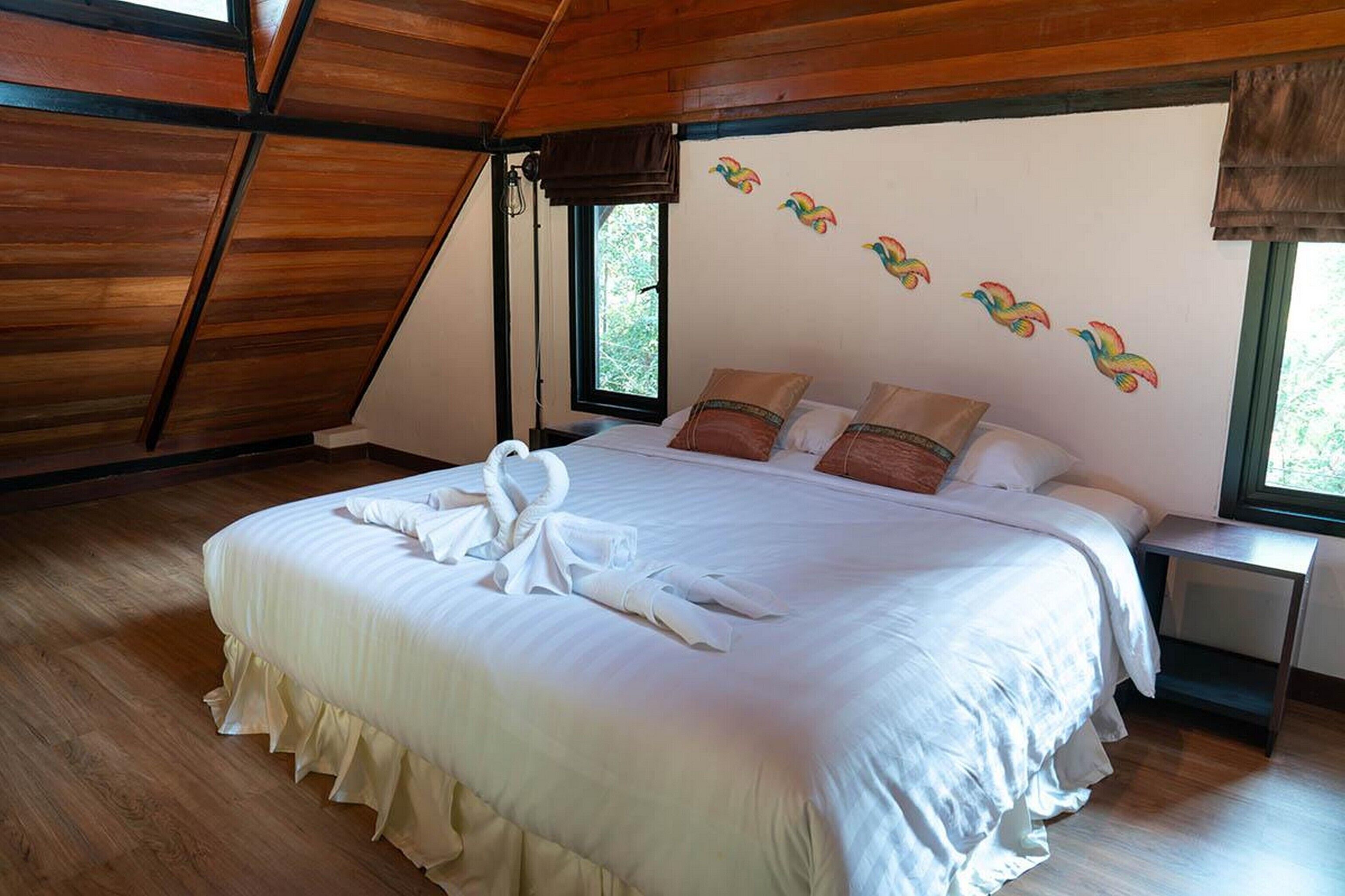 A bedroom with a large bed, wooden ceiling beams, a window, and a wall with colorful bird decals.