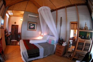 Una habitación con cama, una mesita de noche de madera, un espejo y una estantería con varios objetos.