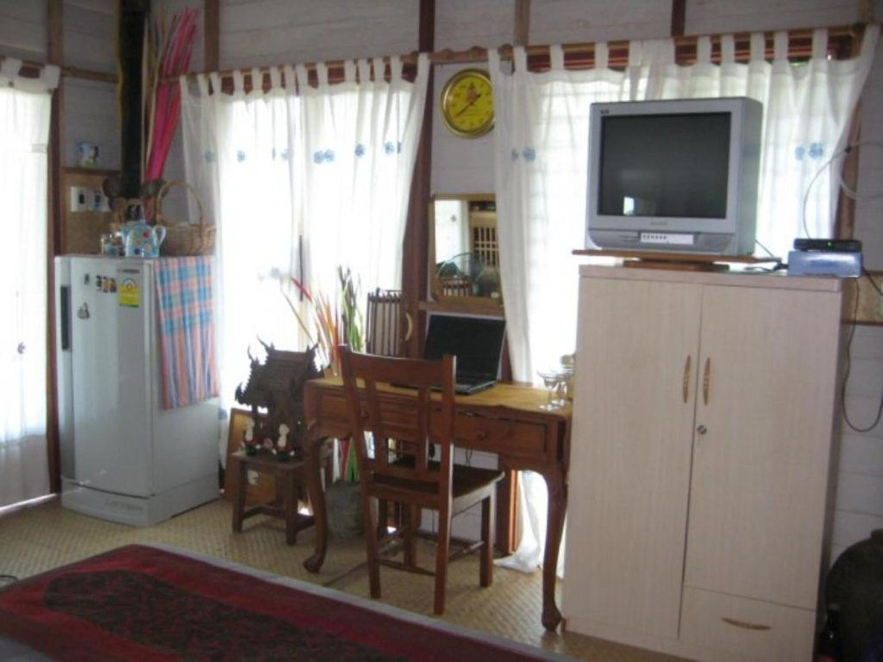 Un espacio habitable compacto con una mesa de comedor, sillas, un refrigerador, un televisor sobre un mueble y un reloj en la pared.