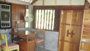 Une pièce avec une table à manger en bois, deux chaises, un ventilateur et une grande porte en bois.