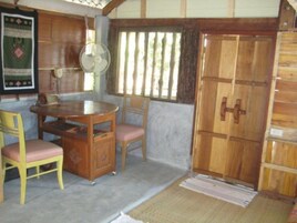 Una habitación con una mesa de comedor de madera, dos sillas, un ventilador y una puerta grande de madera.