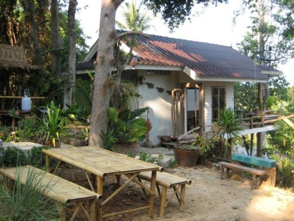 A rustic house with a tiled roof, surrounded by lush greenery and a sandy ground. - Lanlay Homestay (Ao Luek)