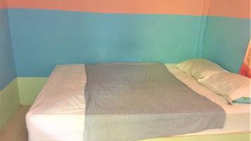 Una cama con una manta gris y almohadas blancas en una habitación con paredes de colores pastel.