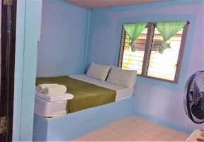 Una habitación pequeña con cama individual, ventana y ventilador.