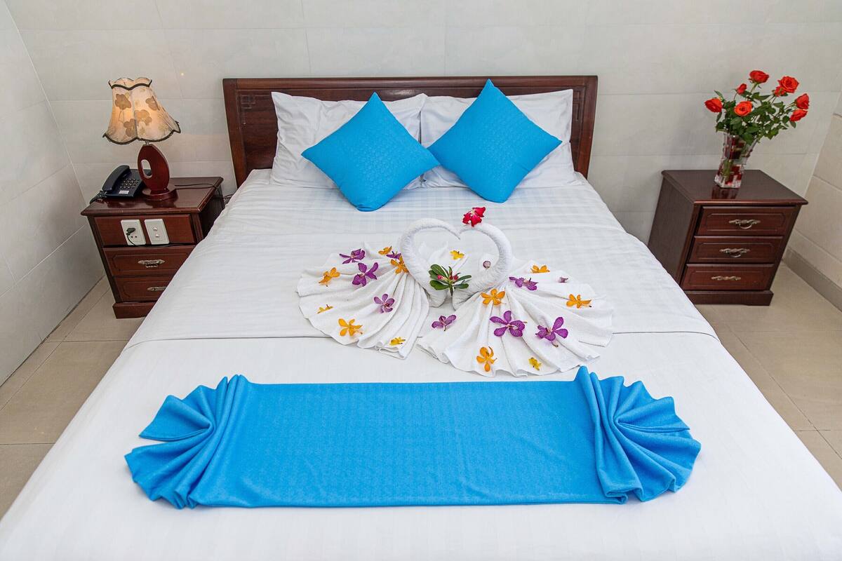 A neatly made bed with blue pillows, a floral towel arrangement, and a blue bedspread.