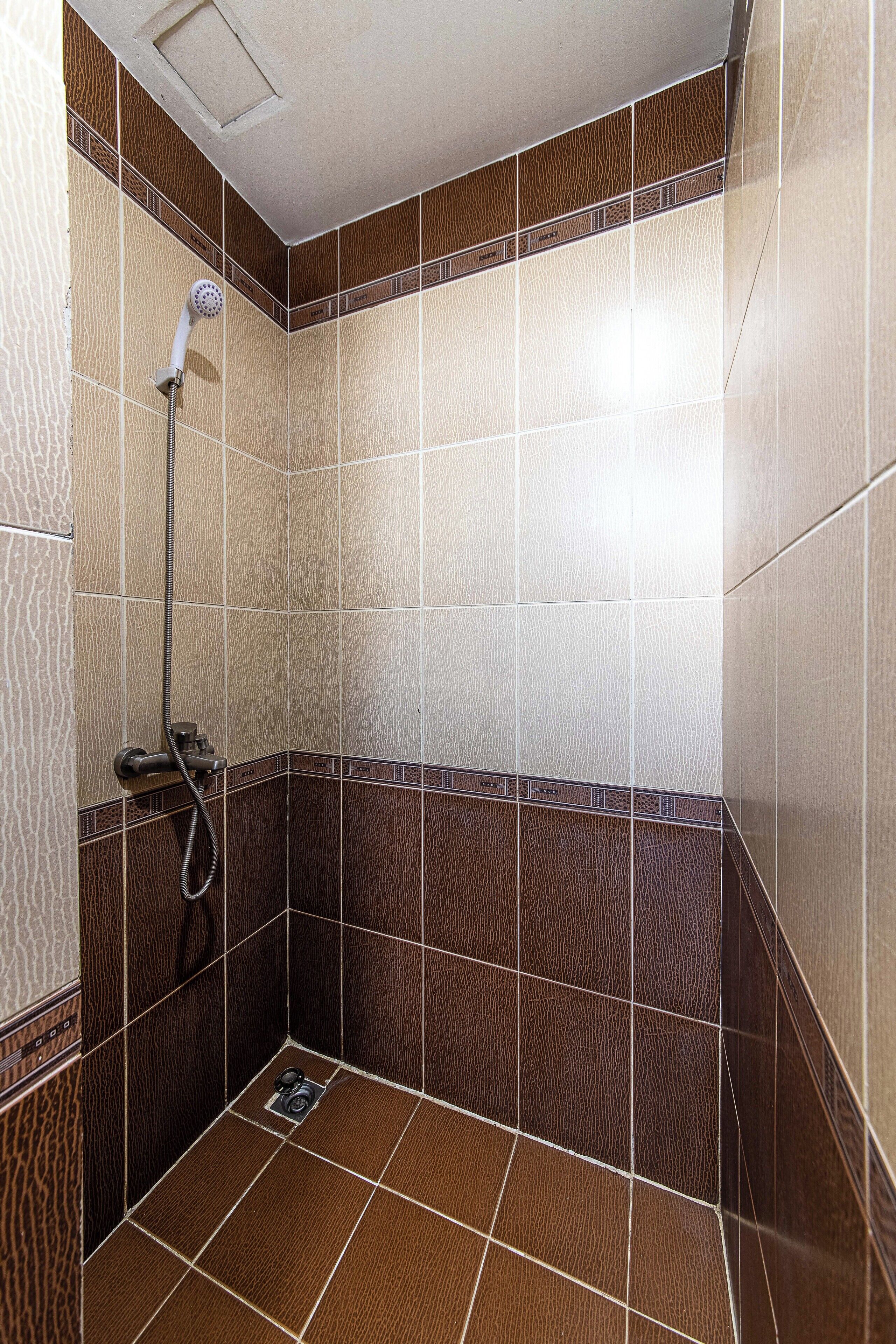 A shower area with tiled walls and floor, a showerhead, and a handheld shower attachment.