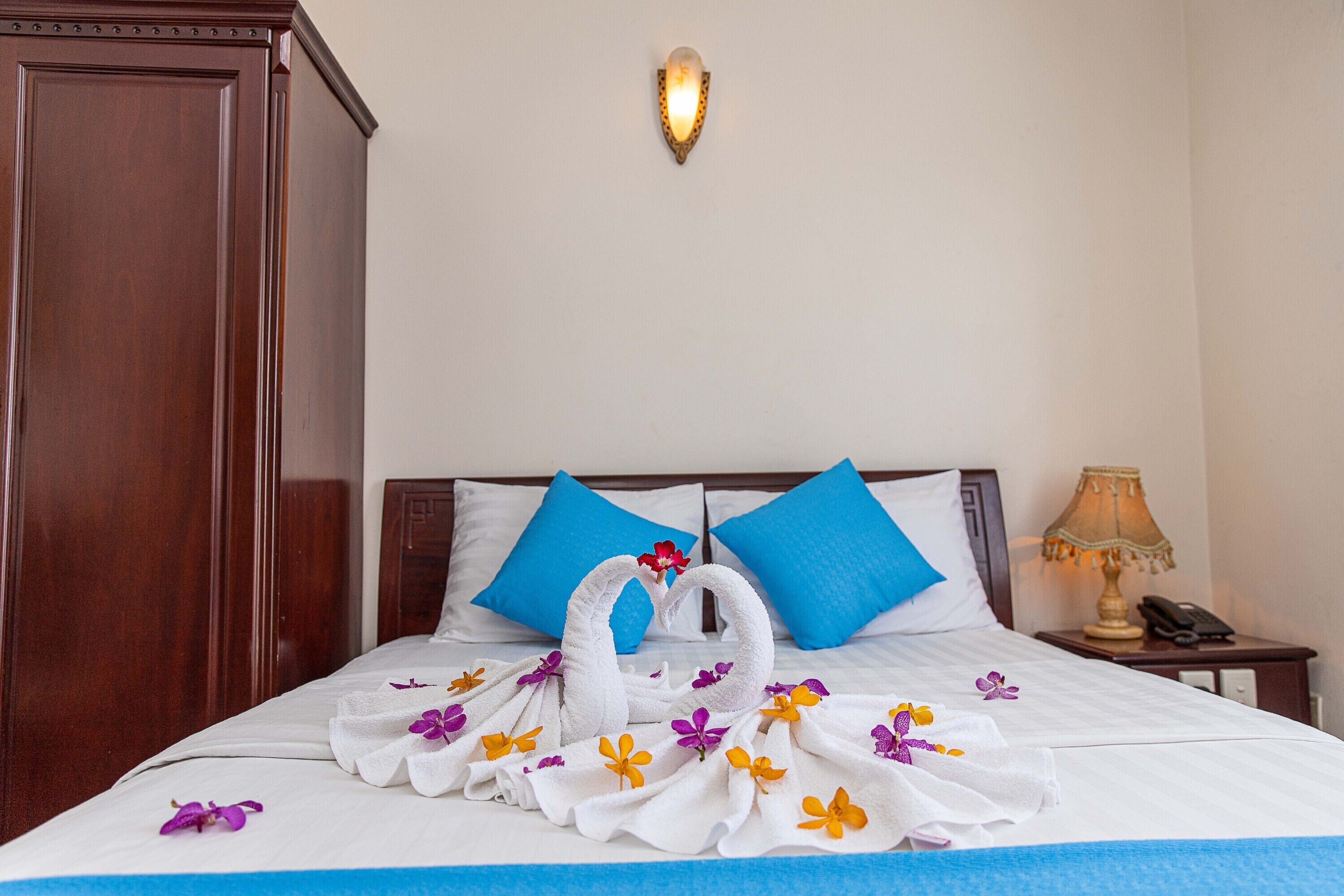 A neatly made bed with blue pillows, a wooden wardrobe, a bedside lamp, and a wall-mounted light fixture.
