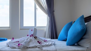 A neatly made bed with white linens and a towel, blue pillows, and a window with curtains. - Phong Lan 2 Hotel (Ho Chi Minh City)
