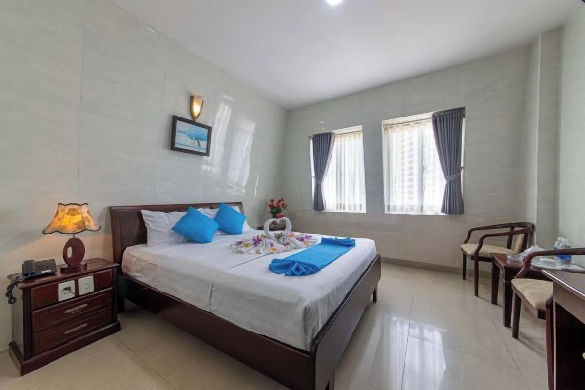 Una habitación de hotel con cama, mesita de noche, lámpara y escritorio con sillas.