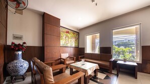 A modern lounge area with wooden furniture, a large vase with red flowers, and a window with a view of greenery. - Phong Lan 2 Hotel (Ho Chi Minh City)