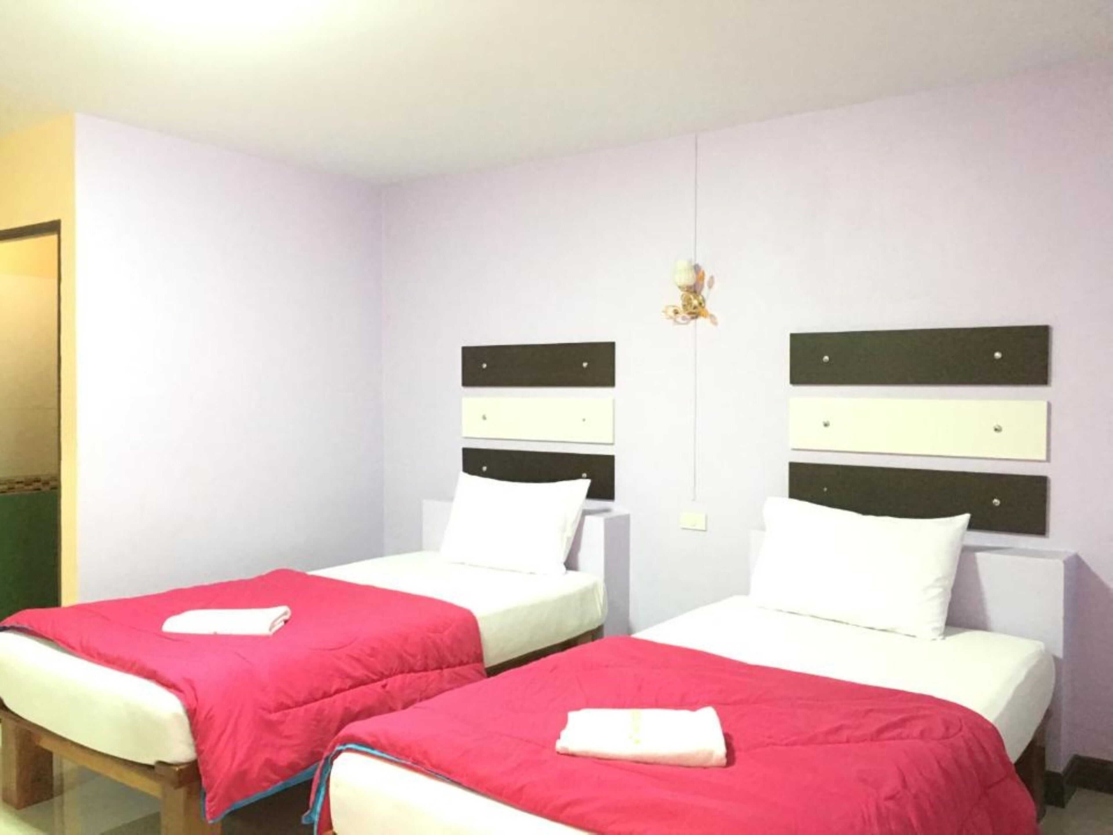 A hotel room with two single beds, each with a white mattress and a red blanket.