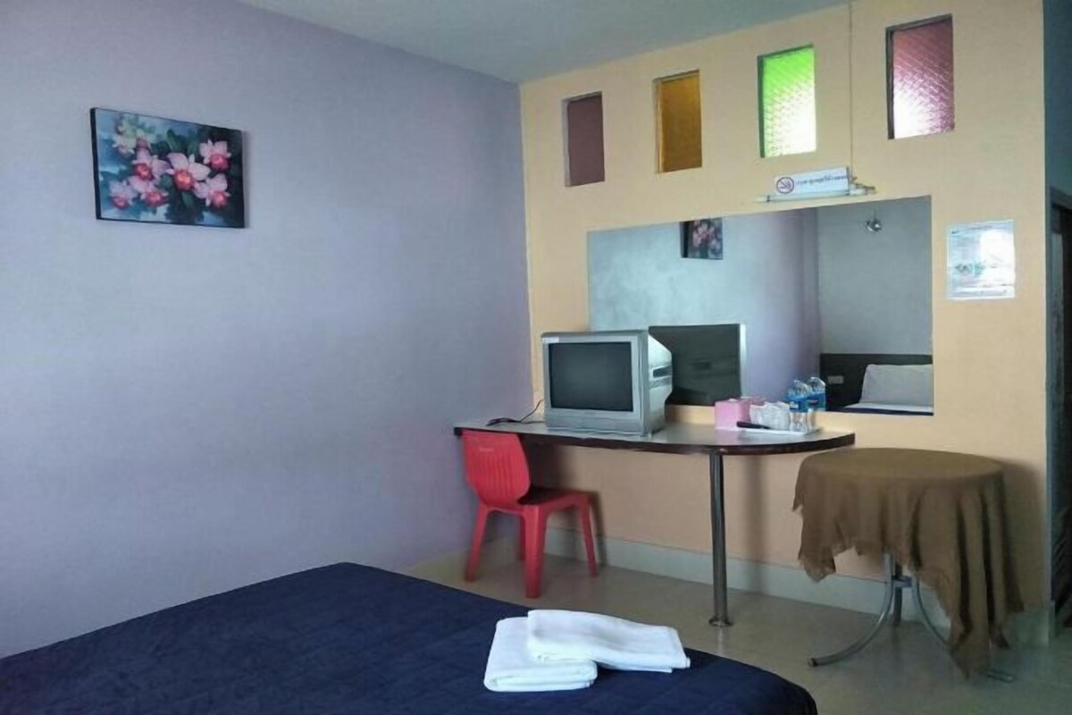 A room with a bed, a desk with a computer, a chair, and a table with a tablecloth.