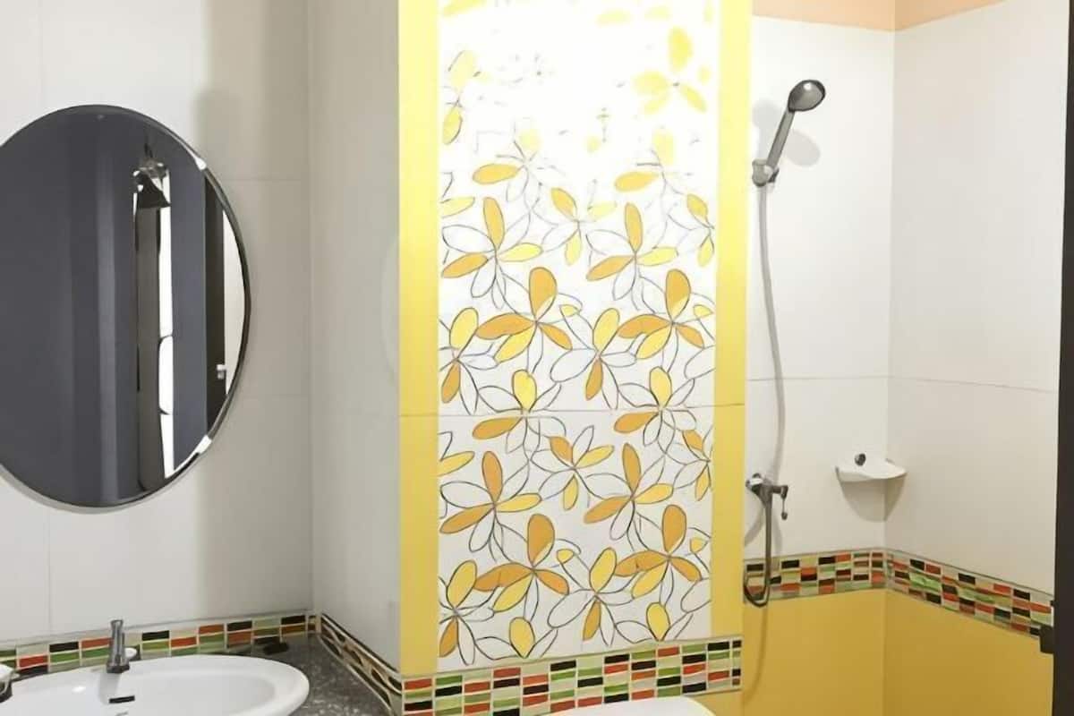 Une salle de bain avec un miroir rond, un lavabo, une douche avec un pommeau de douche amovible et un mur décoratif orné d’un motif floral.
