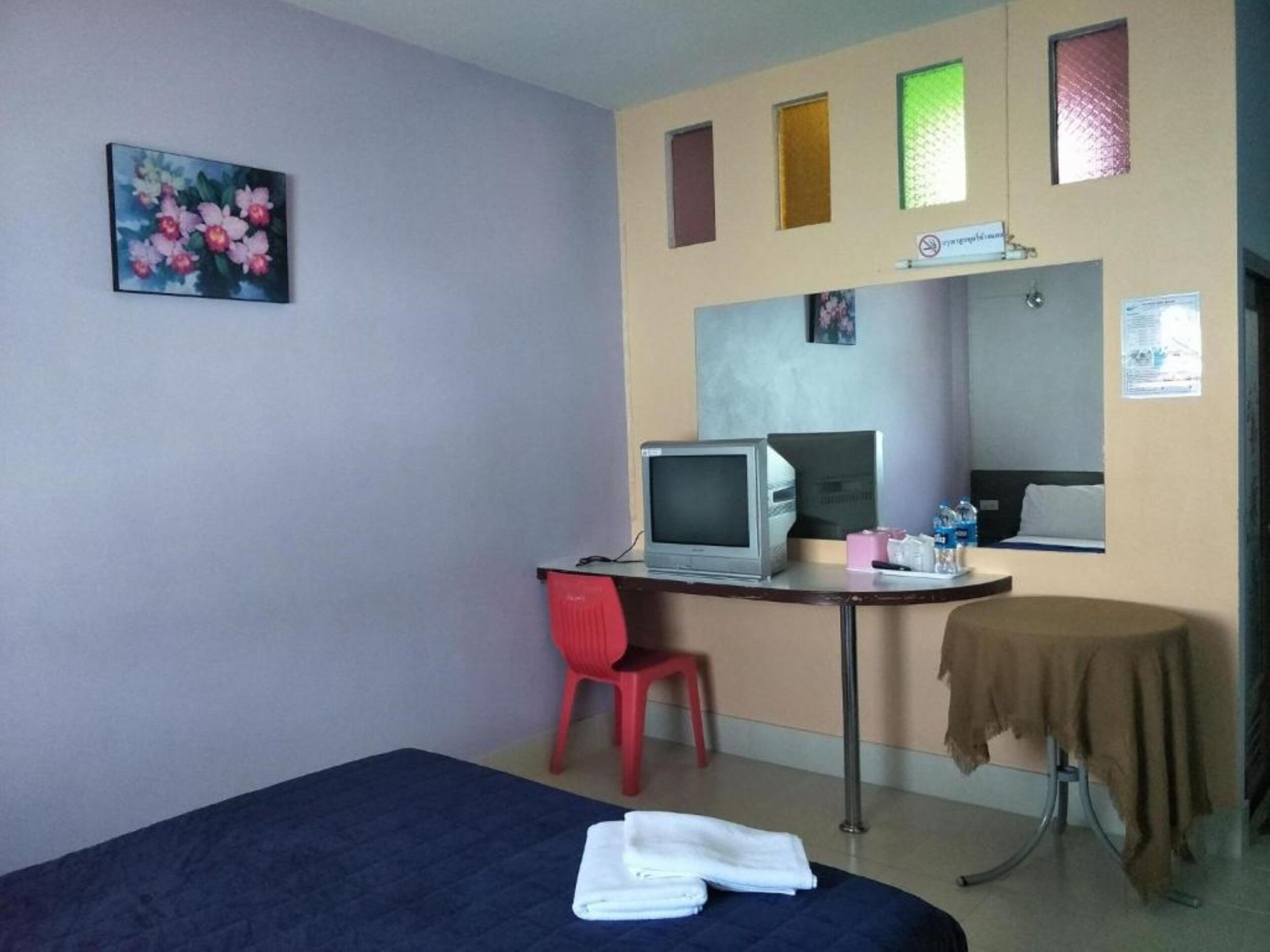 Una habitación de hotel con una cama, un escritorio con una computadora, una silla, una mesita con mantel y un cuadro en la pared.