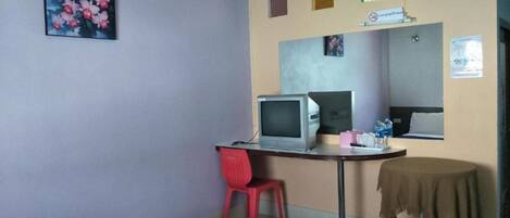 Una habitación de hotel con una cama, un escritorio con una computadora, una silla, una mesita con mantel y un cuadro en la pared.