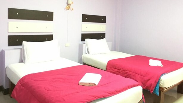 Een hotelkamer met twee bedden, elk voorzien van een wit matras en een rode deken. Er zijn wandlampen op wandgemonteerde nachtkastjes.