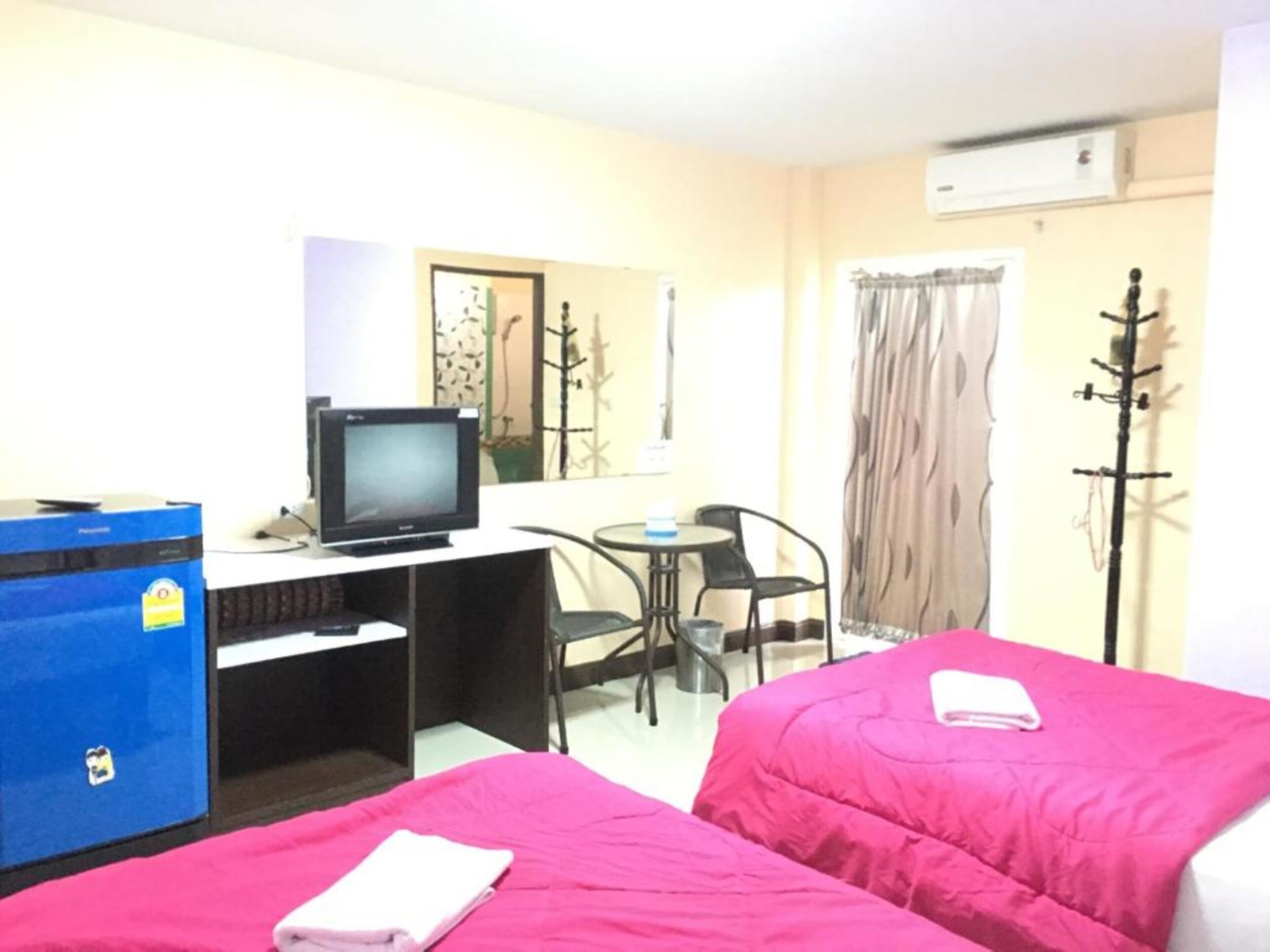A hotel room with two beds, a desk with a computer and a television, a chair, and a coat rack.