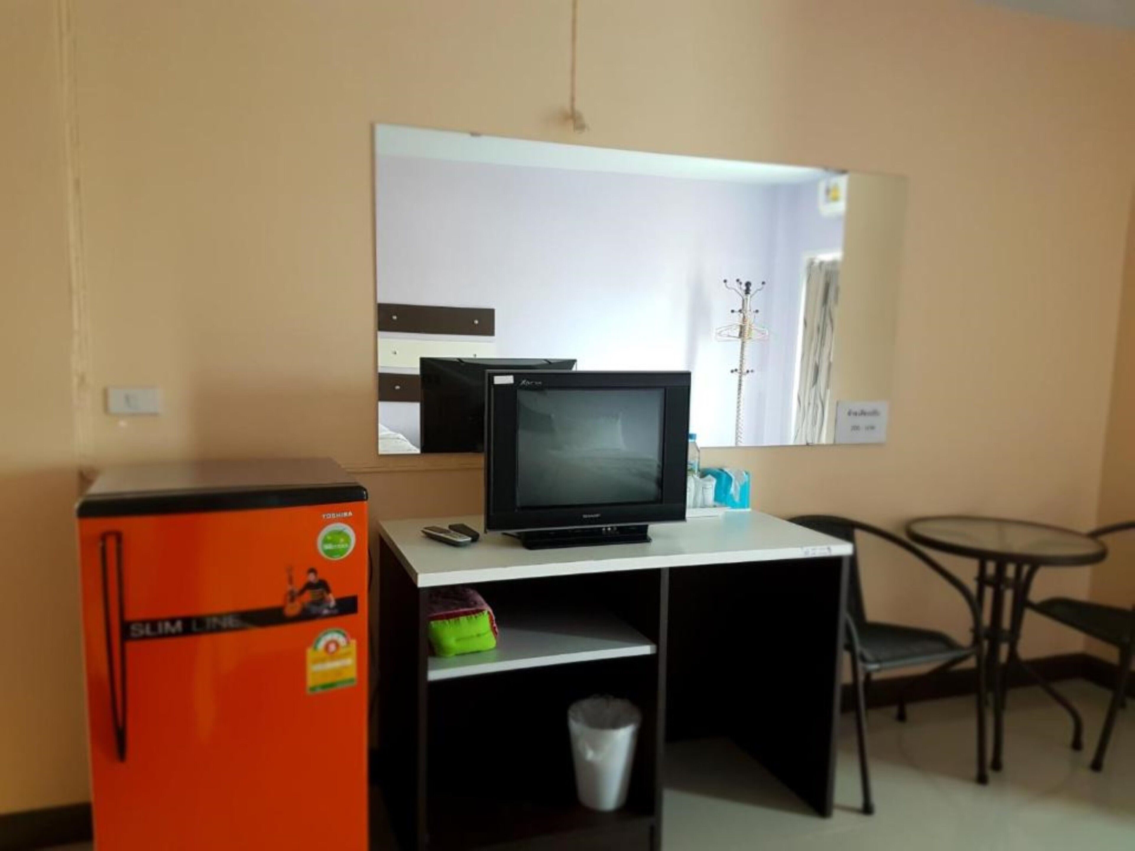 Een kleine hotelkamer met een bureau, een koelkast, een televisie en een stoel.
