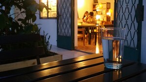 A glass of water on a wooden table with a view of a dining area and a building in the background.