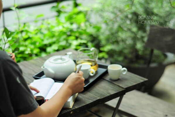 Una persona escribe en un cuaderno sobre una mesa de madera, con un hervidor, tazas y una bandeja.