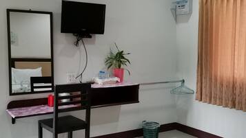 Habitación de hotel con escritorio, silla, espejo, televisor, planta en maceta y ventana con cortinas.