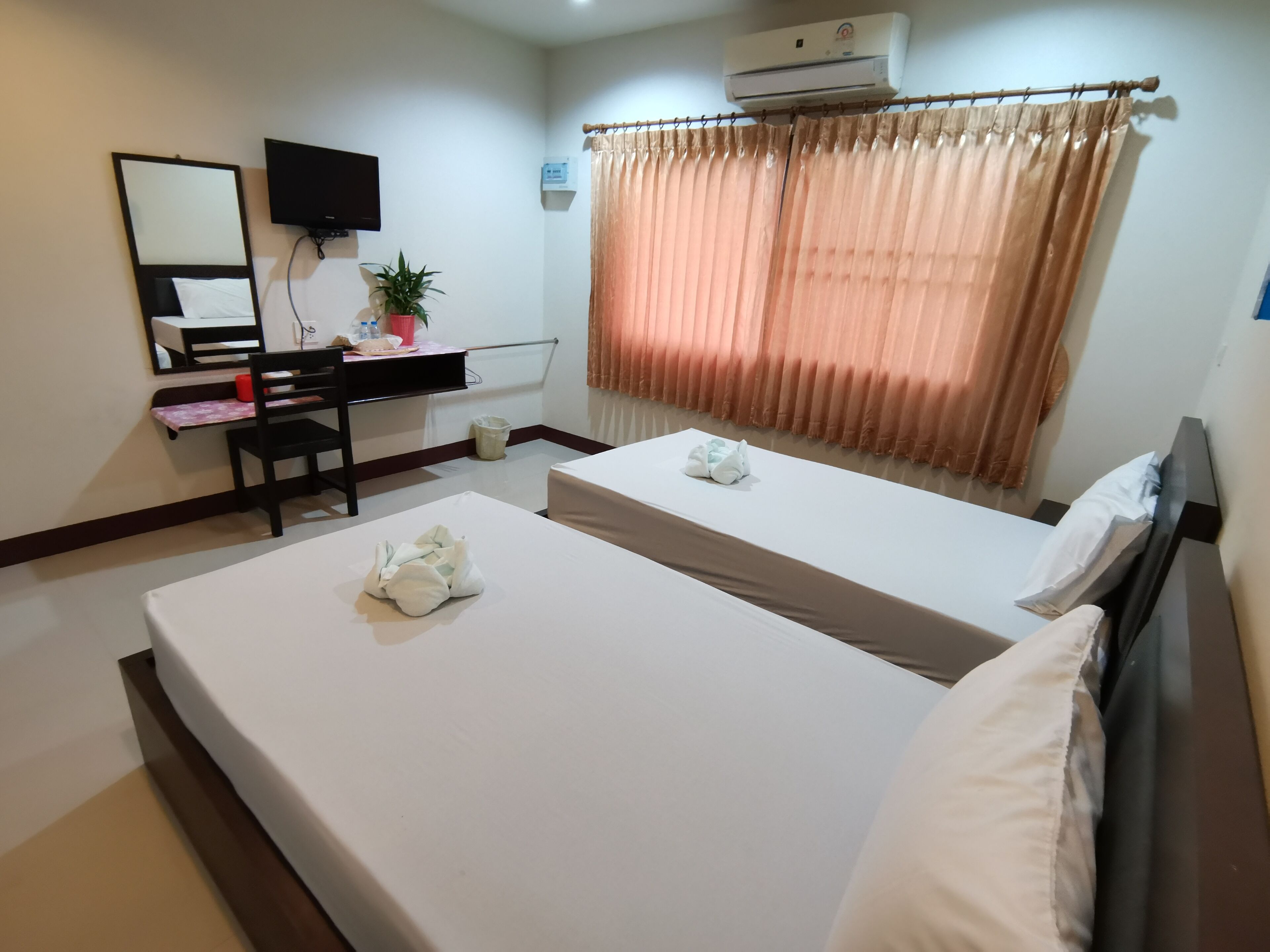 Une chambre d’hôtel avec deux lits, un bureau, une chaise, une télévision, un climatiseur et une fenêtre avec des rideaux.