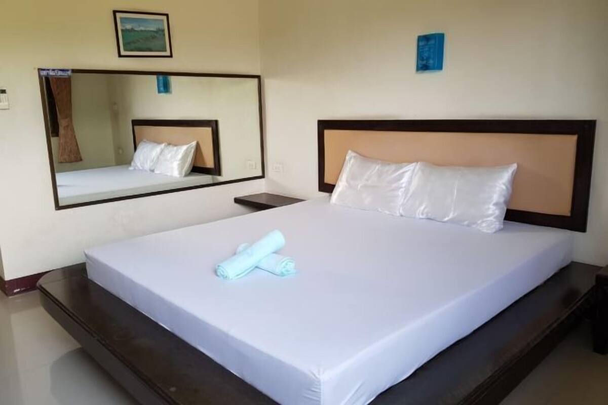 Een hotelkamer met een bed, nachtkastje, spiegel en een aan de muur hangend schilderij.