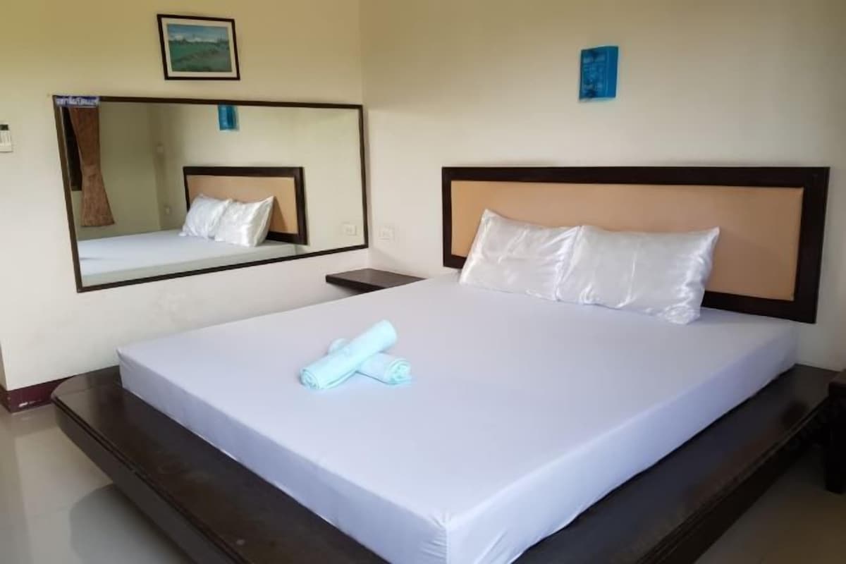 A hotel room with a bed, a nightstand, a mirror, and a wall-mounted picture.
