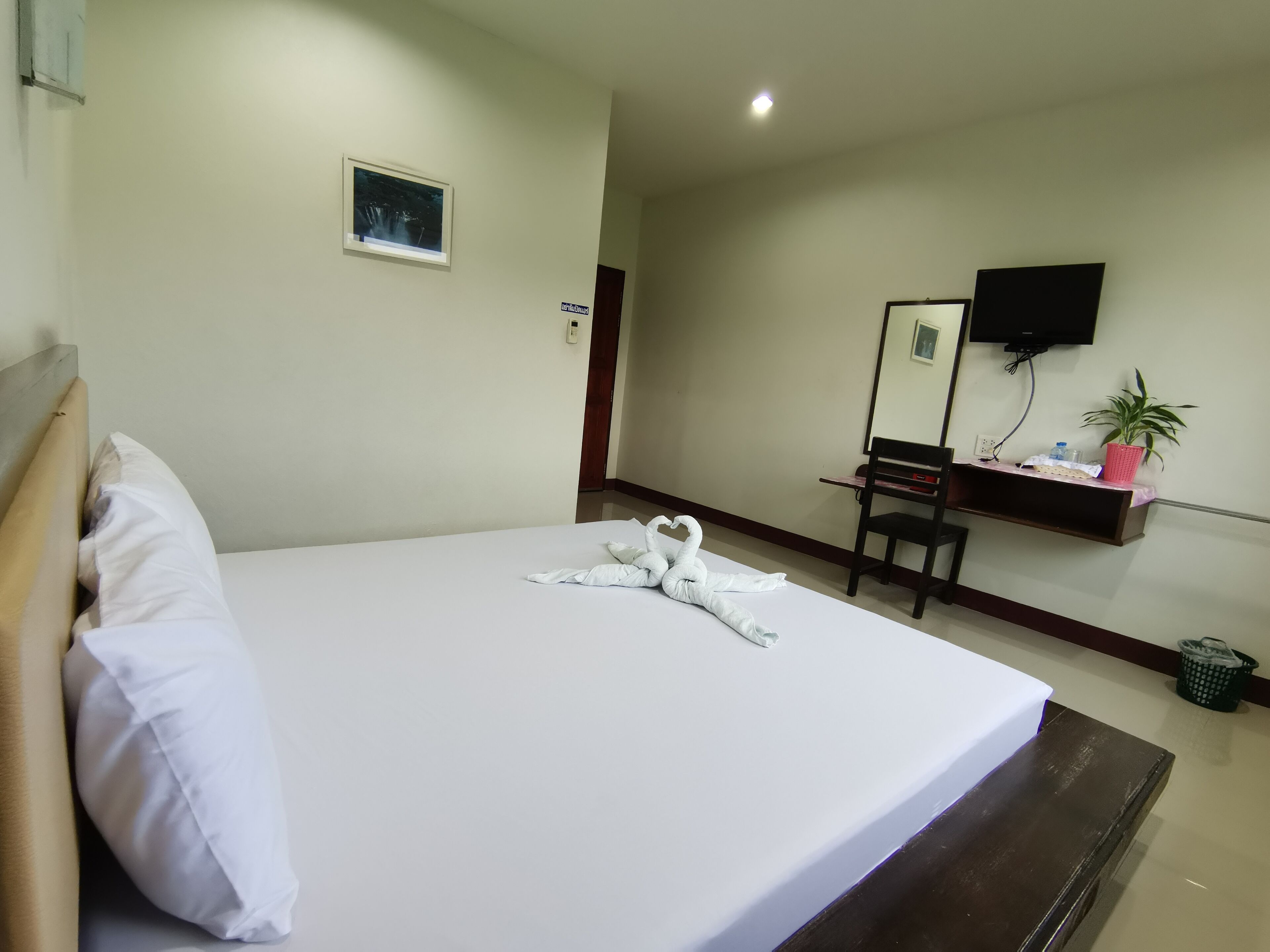 Une chambre d’hôtel avec un lit bien fait, un bureau avec une chaise, une télévision et une petite plante.