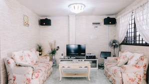 Un salon avec deux canapés à motifs floraux, une table basse, un téléviseur et un ventilateur.