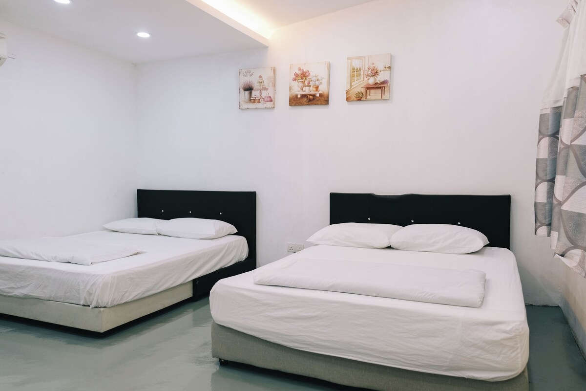 A modern hotel room with two single beds, a large window, and a wall decorated with three floral paintings.