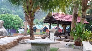A garden area with a stone fountain, palm trees, and a gazebo with a red roof. - Alang Kenari Resort (Yan)