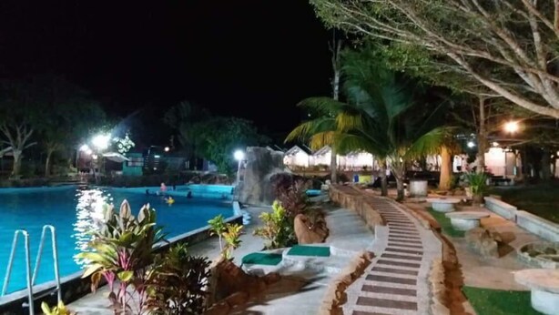 A nighttime pool area with a clear water surface, surrounding plants, and a pathway leading to a building. - Alang Kenari Resort (Yan)