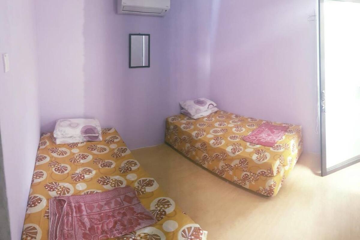 A small, single-room accommodation with two beds, a mirror, and an air conditioning unit.