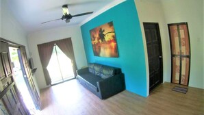 A room with a ceiling fan, a sofa, a painting, and a door. - Alang Kenari Resort (Yan)
