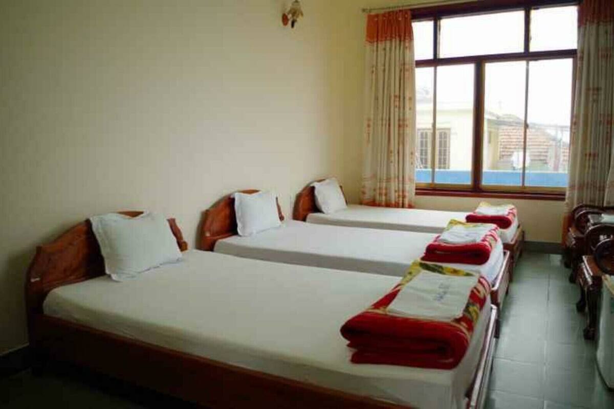 Une chambre d’hôtel avec trois lits simples, chacun doté d’une tête de lit en bois et de draps blancs.