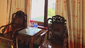 Une pièce dotée d’une grande fenêtre, de deux chaises en bois, d’une petite table avec un plateau en verre et d’un appareil de climatisation placé au-dessus de la fenêtre.