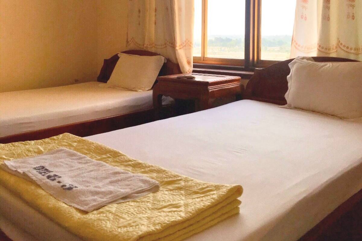 Une chambre avec deux lits simples, une petite table et une fenêtre avec des rideaux.