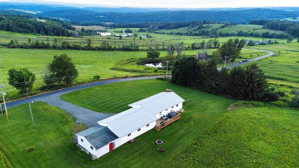A white mobile home with a red door, a deck, and a stone fire pit, surrounded by lush green fields and a winding road. - Peaceful, Family-Friendly Ridge-Top Retreat with Southern Views (Rome)