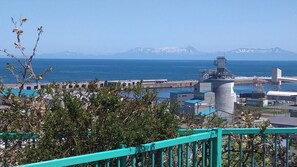 Zona costera industrial con una gran estructura de hormigón, un muelle y montañas al fondo.