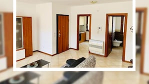Un salon spacieux avec un canapé, une petite table et un coin cuisine visible à travers une porte ouverte.